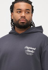 Σκούρα γκρι φούτερ με κουκούλα και τσέπη μπροστά, ρυθμιζόμενο κορδόνι στη�ν κουκούλα και λευκό τυπωμένο λογότυπο στο στήθος. Μαλακό βαμβακερό υλικό με άνετη εφαρμογή.