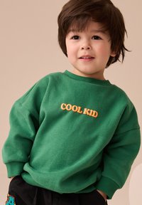 Zöld pulóver narancssárga "COOL KID" hímzéssel, kerek nyakkivágással és hosszú ujjú, puha, texturált anyagból.