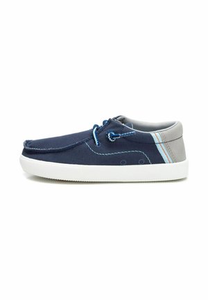 Zapatos de lona azul marino con acentos grises, suela de goma blanca, costuras decorativas y cordones azules. Diseño simple y de perfil bajo.