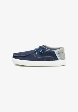 Zapatos de lona azul marino con acentos grises, suela de goma blanca, costuras decorativas y cordones azules. Diseño simple y de perfil bajo.