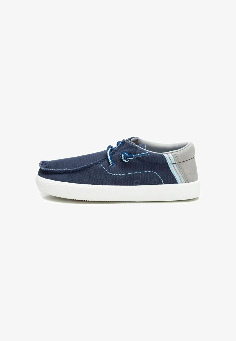 Zapatos de lona azul marino con acentos grises, suela de goma blanca, costuras decorativas y cordones azules. Diseño simple y de perfil bajo.