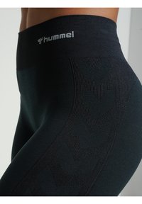 Leggings neri con una ampia vita e il logo "hummel", realizzati in tessuto testurizzato con un motivo a chevron lungo i lati.