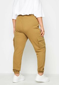 Tannfärgade cargojoggers i mjukt tyg, med en elastisk midja, samlade fållar och sidofickor. Bärs med vita sneakers.