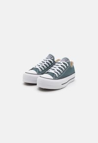 Grüne Canvas-Sneaker mit weißen Gummisohlen und Schnürsenkeln, mit einer runden Zehenpartie, grauem Streifen und einem Logotag auf der Zunge.