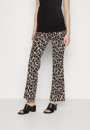 Woman wearing black sleeveless top, leopard print straight-leg pants, and black open-toe block heel sandals standing against white background.