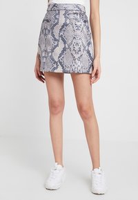 Falda corta con estampado de serpiente en color beige claro y azul marino, con cintura ajustada y textura suave. Estilizada con zapatillas blancas.