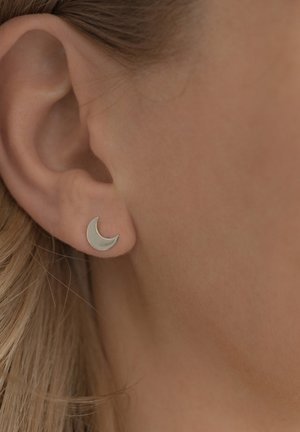 Srebrna obročasta luna stud uho, s gladkom površinom in minimalističnim dizajnom, ki poudarja svojo ukrivljeno obliko.