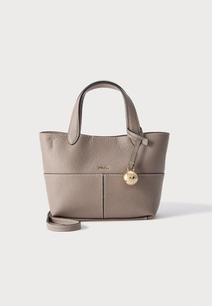 Sac à main en cuir texturé taupe avec double anse, une bandoulière amovible et un pendentif rond doré à l'avant sur un fond clair uni.