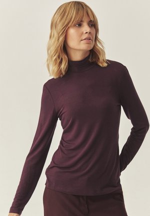 Dolgimi rokavi turtleneck zgoraj v temno burgundski barvi, narejen iz mehkega, raztegljivega blaga, s prilagojeno silhueto in gladko teksturo.