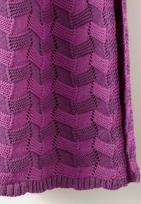 Tissu tricoté violet avec des motifs en chevron alternés et des rangées texturées, montrant un travail de point détaillé et un ourlet côtelé.
