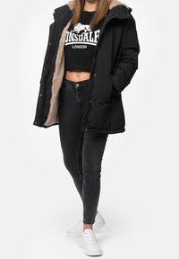 Svart puffjacka med en pluffsig ljusgrå foder, kombinerad med en kort svart T-shirt, mörka jeans och vita sneakers.