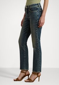 Donkerblauwe rechte jeans van denim, met een licht vervaagde afwerking, vijf zakken en gele steken als accent.