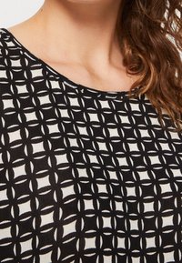 Schwarzer und weißer Stoff mit einem gitterartigen Muster, das abwechselnde Formen und Texturen zeigt. Runder Ausschnitt und glatte Textur.