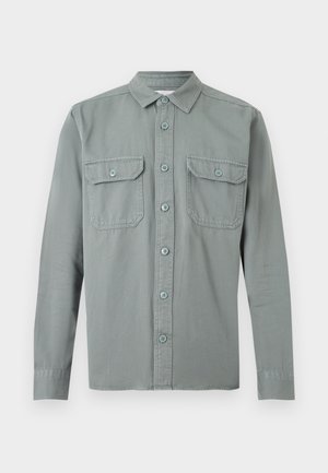 Šviesiai pilka ilgomis rankovėmis palaidinė su atsegamais mygtukais, apykakle ir dviem krūtinės kišenėmis su lipukais, išdėstyta plokščiai ant balto fono.