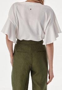 Hvid kortærmet top med flagrende ærmer og en lille hardwaredetalje på ryggen, parret med olivengrønne højtaljede bukser med baglommer.