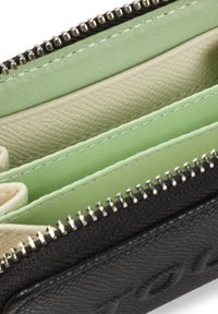Cartera negra con cremallera, con múltiples compartimentos, hecha de cuero texturizado y tela lisa. Presenta forros interiores en verde claro y beige.