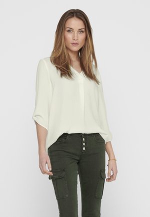 Cream-colored, V-neck blouse with three-quarter sleeves, paired with olive green cargo pants featuring buttoned front and side pockets.