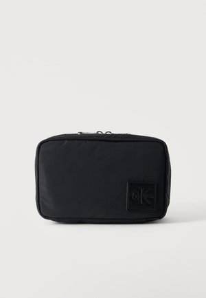 Sort rektangulær lynlåset pung med et lille præget Calvin Klein-logo mærke på fronten, sat mod en ensfarvet baggrund.