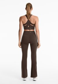 Ensemble de sport marron comprenant un soutien-gorge de sport avec découpe au dos et des leggings évasés taille haute. Texture lisse et design ajusté.