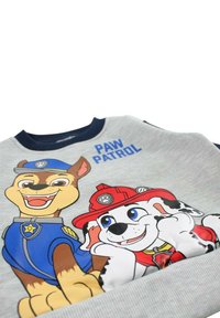 Sweat-shirt gris avec des chiens dessinés de "Paw Patrol". Le design comprend des accents bleus et rouges avec des illustrations ludiques des personnages.