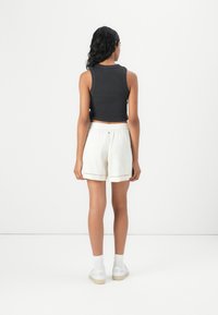 Black cropped tank top paired with light beige shorts featuring decorative trim, white sneakers, and white socks. Simple, casual outfit.