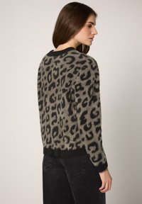 Maglione con stampa leopardata in grigio con macchie nere, texture morbida, scollo rotondo e maniche lunghe; abbinato a jeans scuri.