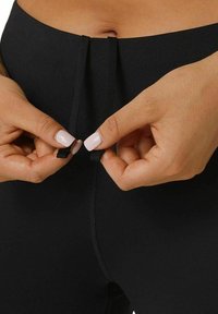 Black high-waisted leggings featuring a flat waistband with a double tie for adjustment, made from a smooth, stretchy fabric.