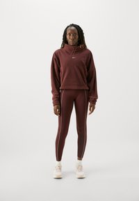 Bordeauxfarbener Hoodie mit hohem Kragen und Logo, kombiniert mit passender Leggings mit weißen Seitenstreifen. Helle Sneakers.