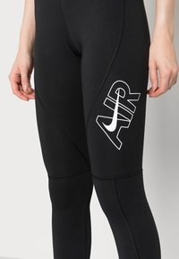 Czarne legginsy sportowe z białym logo "AIR" i charakterystycznym znakiem Nike. Gładki materiał z kontrastowymi szwami i dopasowany design.