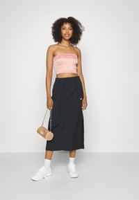 Top rosa com pregas sem alças, saia preta até ao tornozelo com fendas laterais, sapatilhas brancas e uma pequena bolsa redonda bege com alça de corrente.