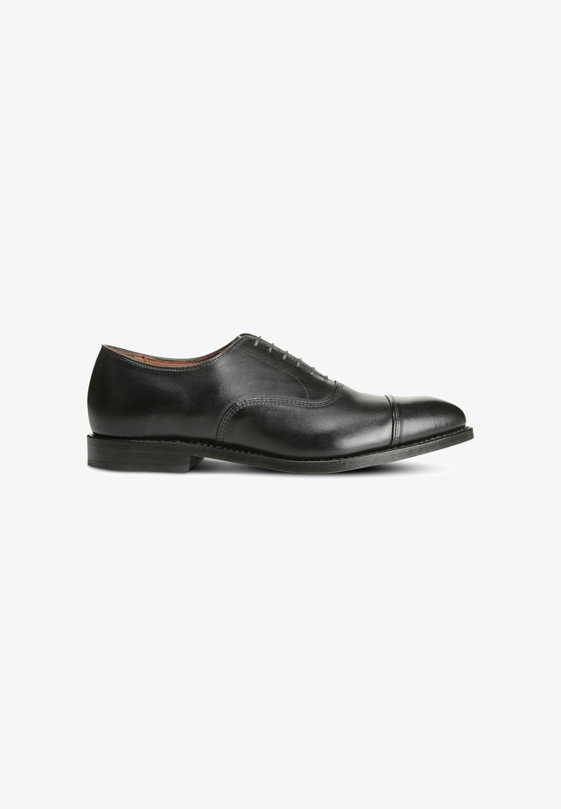 Chaussure habillée en cuir noir avec une finition lisse, un bout rond, cinq œillets pour les lacets et un petit talon empilé. Présente des détails de couture subtils.