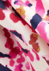 Tissu satin présentant un motif abstrait rose et rouge sur un fond crème. La texture est lisse avec des contrastes de couleurs vives.