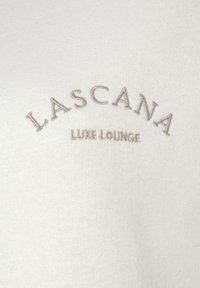 Sweatshirt beige clair avec une texture douce, ornée de "Lascana Luxe Lounge" brodé en brun clair sur le thorax dans un design en arc.