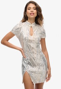 Robe courte en sequins argentés avec un col haut, un décolleté en forme de clé et une fente sur le côté. Présente un motif géométrique et une silhouette ajustée.