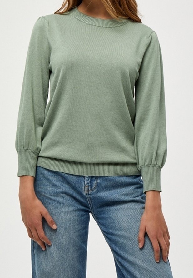 Maglione verde chiaro con scollo rotondo a coste, maniche lunghe a palloncino e polsini a coste. Indossato con jeans blu in denim.