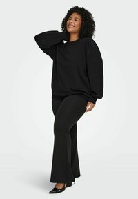 Črna jopa s nabranimi rokavi in cvetličnimi izrezljanimi detajli, kombinirana s črnimi razširjenimi hlačami in čevlji z ostrim nosom.