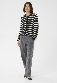 Juodai balta juostelėm kardiganas su tekstūruotu paviršiumi, sagutėmis priekyje ir juoda apykakle, derinamas su aukštu liemeniu pilnais džinsais.