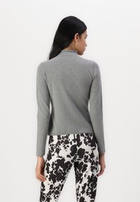 Light grey sweater with a high neckline and long sleeves, made of soft material. Paired with black and white patterned pants.