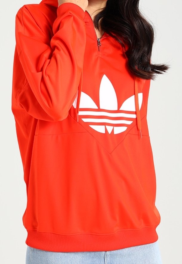 Red pullover hoodie with a half-zip, featuring a large white Adidas logo. Made from smooth material, it has a front kangaroo pocket and ribbed cuffs.