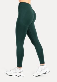 Grüne Leggings mit hoher Taille, glatter Textur und nahtlosem Design, kombiniert mit weißen, klobigen Sportschuhen und gemusterten Knöchelsocken.