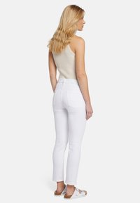Jeans blancs taille haute avec une coupe droite, en coton, poches arrière discrètes, associés à un débardeur beige côtelé et des sandales légères.