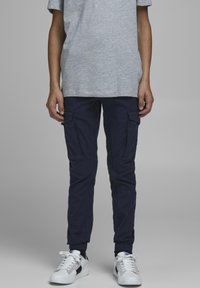 Navy cargo-byxor med elastiska muddar, med flera sidofickor, ihop med en grå t-shirt med kort ärm och vita sneakers.