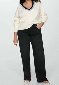 Pull crème en v avec bordures noires et bleues, associé à un jean noir taille haute à jambes larges. Le matériau semble doux, avec une coupe décontractée.