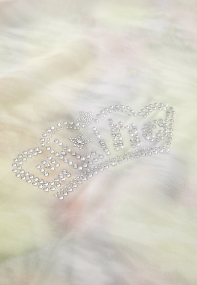 Pasteļa krāsas audums ar mirdzošu kristālu dizainu, kas veido vārdu "mans" un kroni, ar zvaigznēm, kas akcentē tekstu.