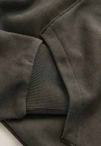 Tissu de sweat-shirt gris foncé avec des textures lisses et côtelées au niveau de la poche. Détail de couture notable le long des bords.