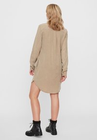 Beige långärmad skjortklänning med en böjd fåll, sidofickor och knäppmanchetter, i kombination med svarta ankelstövlar. Mjuk texturerad tyg.