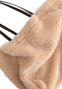 Beige fuskpäls tote bag med en mjuk, texturerad yta och mörkbruna remmar. Har en rymlig design och sömlösa kanter för ett stiligt utseende.