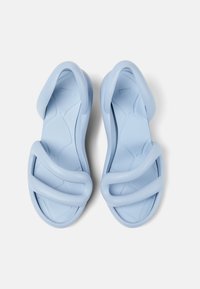 Vaaleansiniset kumisaappaat, joissa on kaksi leveää hihnaa, teksturoitu pohja ja muotoiltu rakenne. Silkkinen pinta ja minimalistinen muotoilu.