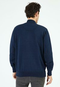 Pull bleu marine à manches longues, avec des poignets et un ourlet côtelés. Présente des empiècements texturés au niveau des coudes. Matière tricotée douce, design à col rond.