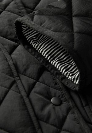 Schwarze gesteppte Jacke mit einem schwarzen Knopf, Fischgrätbesatz und einem gestreiften schwarz-weißen Innenfutter. Strukturiertete Außenseite.